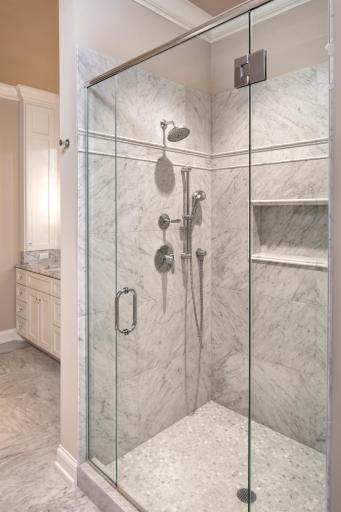 Beautiful tile work, glass and multiple shower heads featured in the owner's shower area