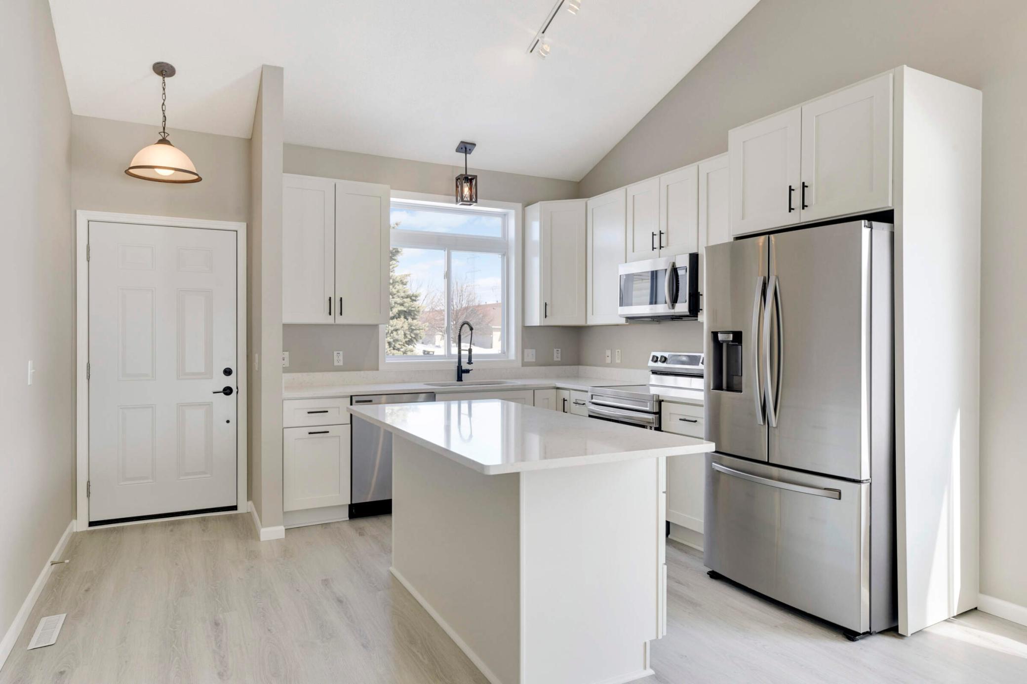 Elegant kitchen features white Shaker cabinets, quartz countertops and SS applainces