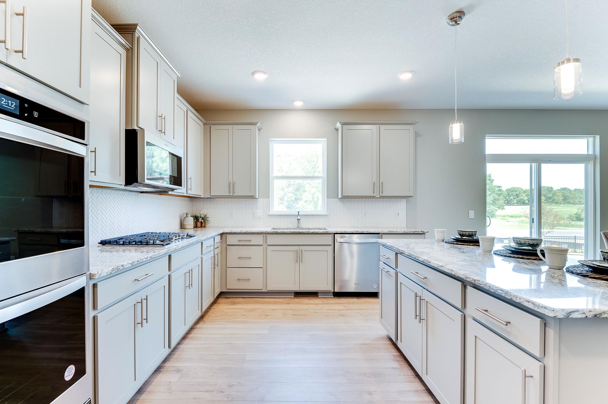 The kitchen of your dreams - complete with stunning Granite countertops, elegant backsplash, modern cabinetry & a stainless steal appliances that'll leave the family chef in their happy place! Photo of model home, color & options will vary.