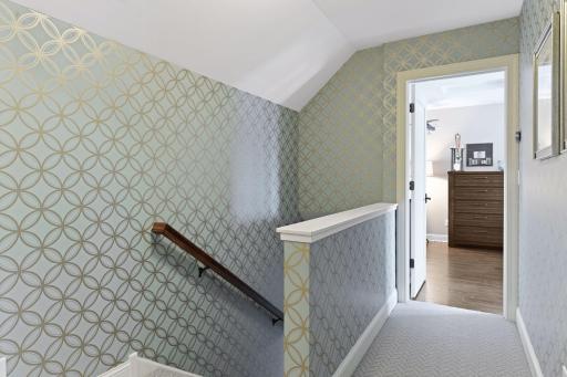 The upper-level hallway leads to both bedrooms, the bathroom, and a small bonus/storage room. The wallpaper-ed staircase and upper level add an elevated touch.