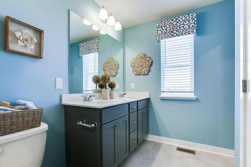 Dual vanity sinks, linen closets and window to allow natural light in primary bath. Photo of model, colors and options will vary.