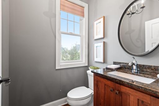 The main floor powder room, located between the mudroom and the foyer features a lovely vanity with granite countertop and ample natural light.