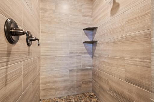 The walk-in shower features dual shower heads and custom tile.