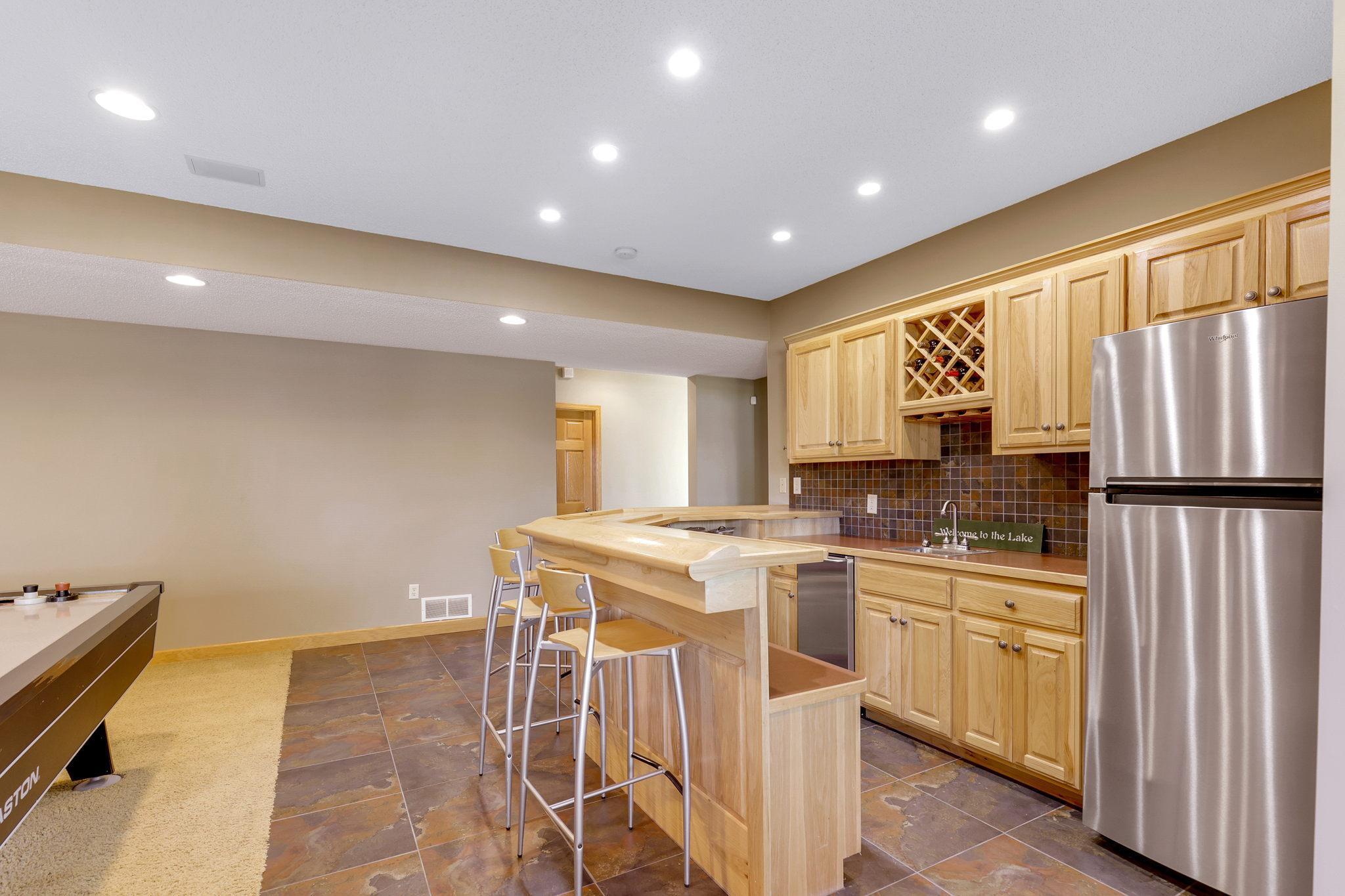 Full far features hickory raised paneled doors, wine bottle display, stemware storage, raised countertop for multiple stools, refrigerator and ceramic tile backsplash / flooring