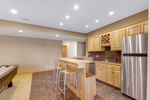 Full far features hickory raised paneled doors, wine bottle display, stemware storage, raised countertop for multiple stools, refrigerator and ceramic tile backsplash / flooring