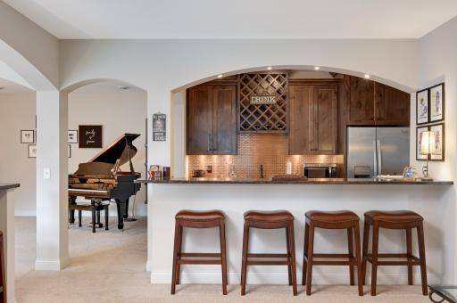 A full wet bar in granite, copper backsplash and refrigerator