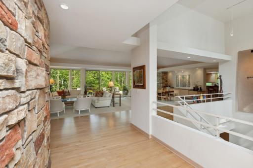 The wilderness, natural light and beauty flows to the interior of this sprawling rambler through floor-to-ceiling windows, towering transom windows, vaulted ceilings, around natural stone on walls, fireplaces, and deck spaces.