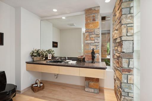 Glass block and stone cascade down the opposing wall in the powder room with granite tops and floating cabinet.