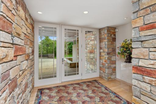 The front entrance, which is soft and inviting, blending the stone from the overhead soffits of the exterior front porch to the interior foyer wall.