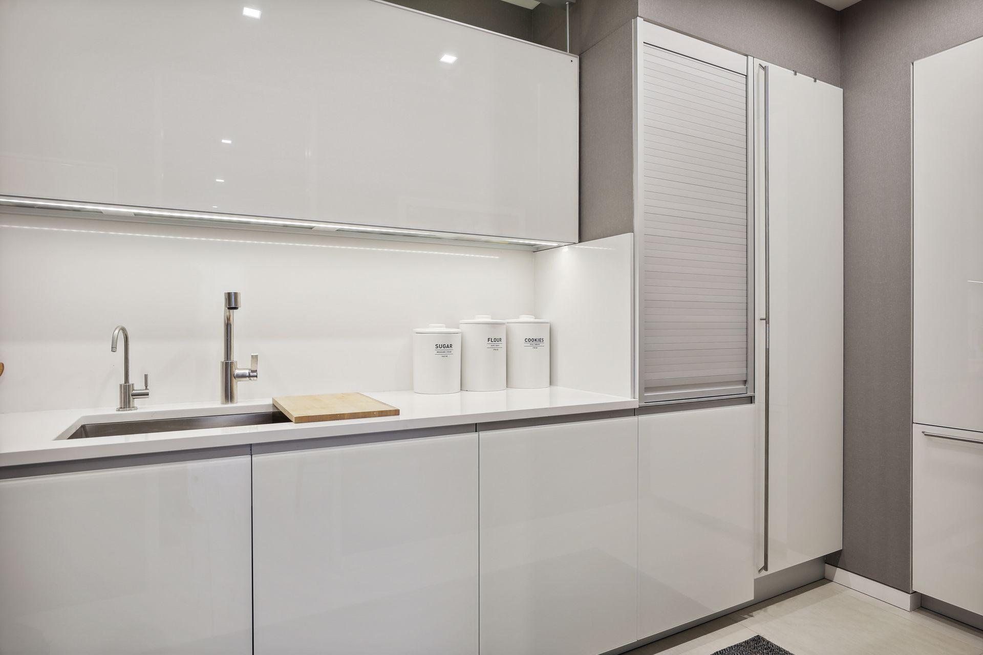 The spacious butler's pantry includes a prep sink, integrated luxury brand appliances including a dishwasher, refrigerator, and freezer, as well as a coffee bar behind the appliance garage, upper and lower cabinetry and a pantry cupboard.