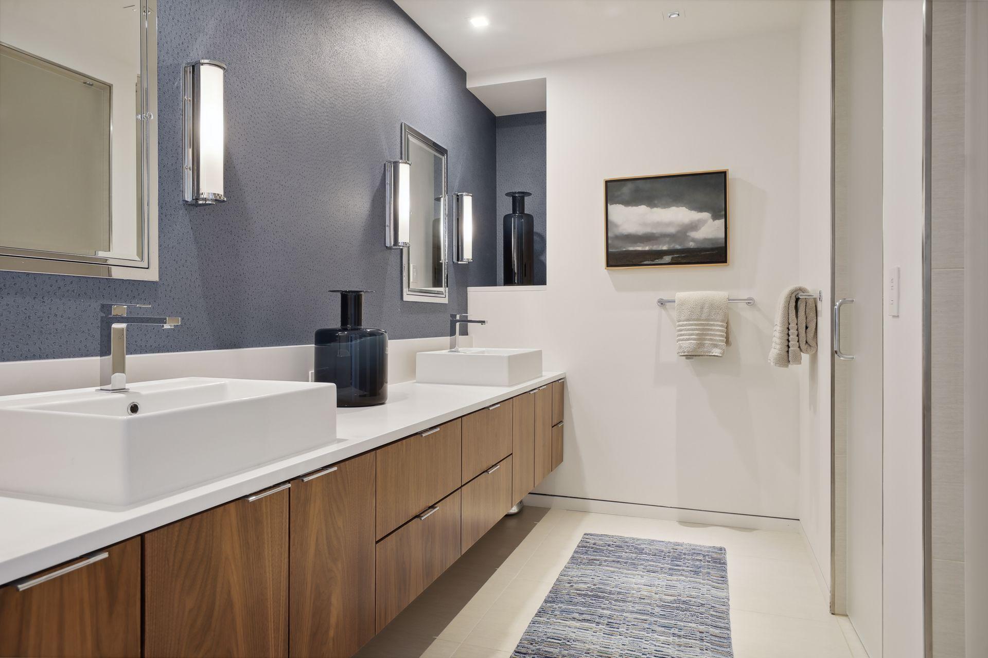 Private en suite bath for the main level bedroom featuring a double vanity, walnut cabinetry, tile floors, medicine cabinets, and etched glass doors to the walk-in shower and separate water closet.