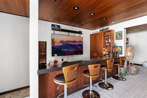 The lower-level family room is set up for entertainment, featuring a full bar/kitchenette and a stone fireplace.