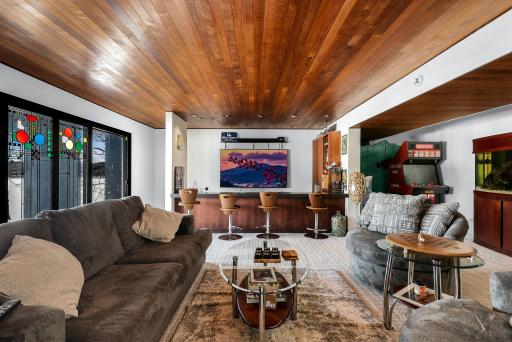 The lower-level family room is set up for entertainment, featuring a full bar/kitchenette and a stone fireplace.