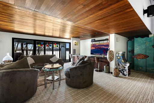 The lower-level family room is set up for entertainment, featuring a full bar/kitchenette and a stone fireplace.