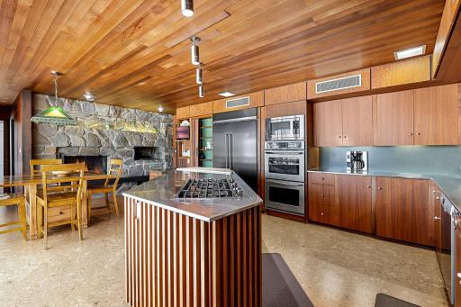 The eat-in kitchen features a walk-in pantry, indoor grill with ventilation, stone fireplace, double wall ovens, stainless counter tops and appliances, cork flooring, custom cabinetry and a 5 burner, gas cooktop.
