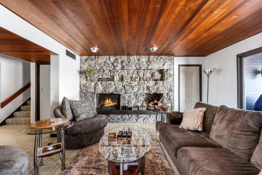 The lower-level family room is set up for entertainment, featuring a full bar/kitchenette and a stone fireplace.