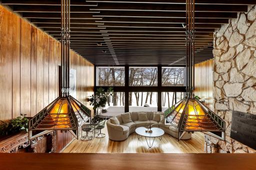 Enjoy stunning views from the living room featuring floor to ceiling windows, custom Frank Lloyd Wright replica lighting, custom Bollenbach stainless steel lighting, a sunk-in seating area with built-ins, 14-foot-tall ceilings and Teak walls.