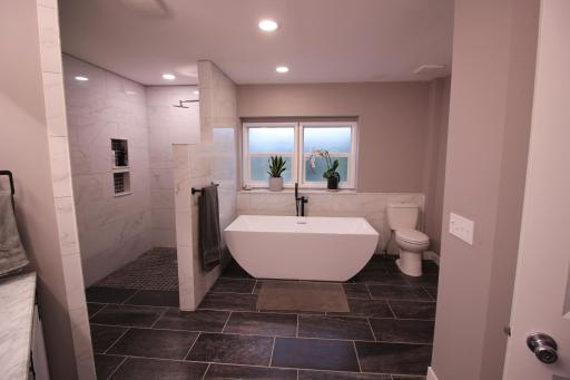 Large free standing soaking tub. Windows look out to the south and has frosted glass for privacy. All toilets are dual flush to save water. Left of the tub is a custom built and tiled roll-in shower.