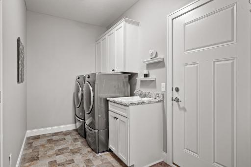 Laundry room and mud room area features built in upper cabinets and a granite laundry sink