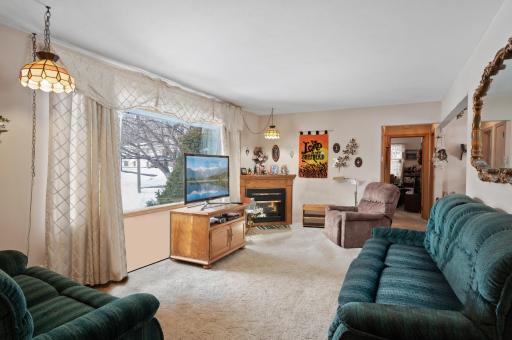 Main level living room features hardwood floors under the carpet, a corner electric fireplace and sunset views from the huge picture window.