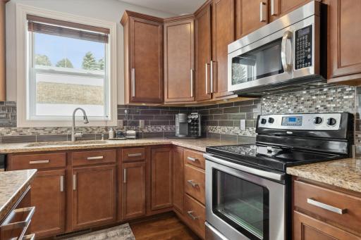 The kitchen features granite countertops, stainless steel appliances, tile backsplash and hardwood floors.