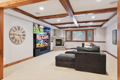 LL family room with box beam ceiling, lookout windows, gas fireplace with natural stone surround. Comfortable setting for movie nights