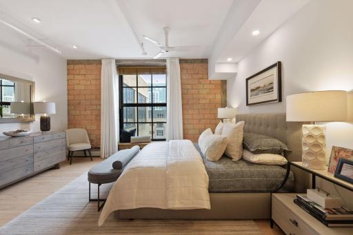 A generous primary suite features hardwood floors, a wall of historic limestone brick, a large operating window, and two closets: a large walk-in closet and a second double door closet.