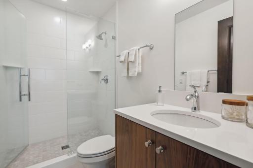 This bedroom has an ensuite three-quarter bath with tile floors, a wood vanity and quartz countertop, and a tiled shower.