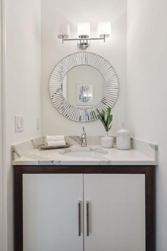 The stylish powder room has a wood pocket door, matching wood and enameled cabinets as the mudroom entry, and quartz countertops.