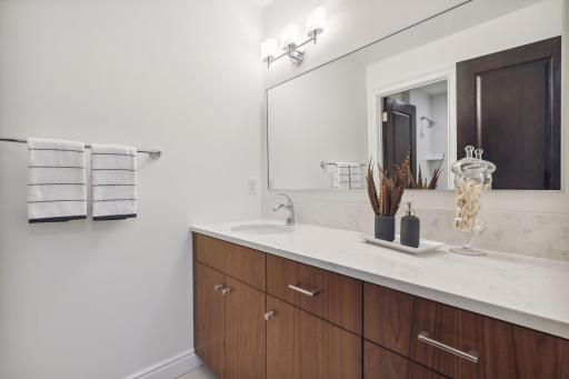 In the hallway, there is a large linen closet and a full bath with a wood vanity, quartz countertop, and a tiled floor. The bath also features a combo shower and tub.