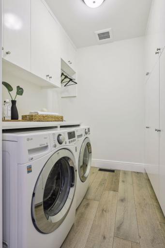 The laundry room is directly off the mudroom coming in from the garage. It has LG front load washer and dryer, a sink, and white enamel cabinets with ample storage space.