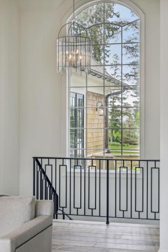 The two-story vaulted staircase has gallery-like features: oversized windows, iron railings, and a beautiful chandelier. The white walls and tall ceilings create the perfect backdrop to hang artwork!
