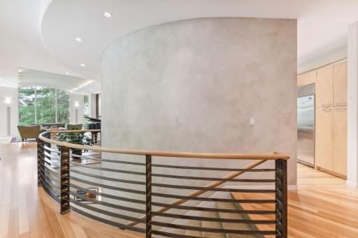A prominent half wall gracefully separates the foyer from the kitchen, its curvaceous form gently embraces a staircase that descends to the lower level, adorned with exquisite iron railings.