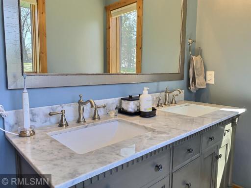 The adjoining bathroom has been remodeled and boasts a double vanity with a grey wash finish and marble countertop.