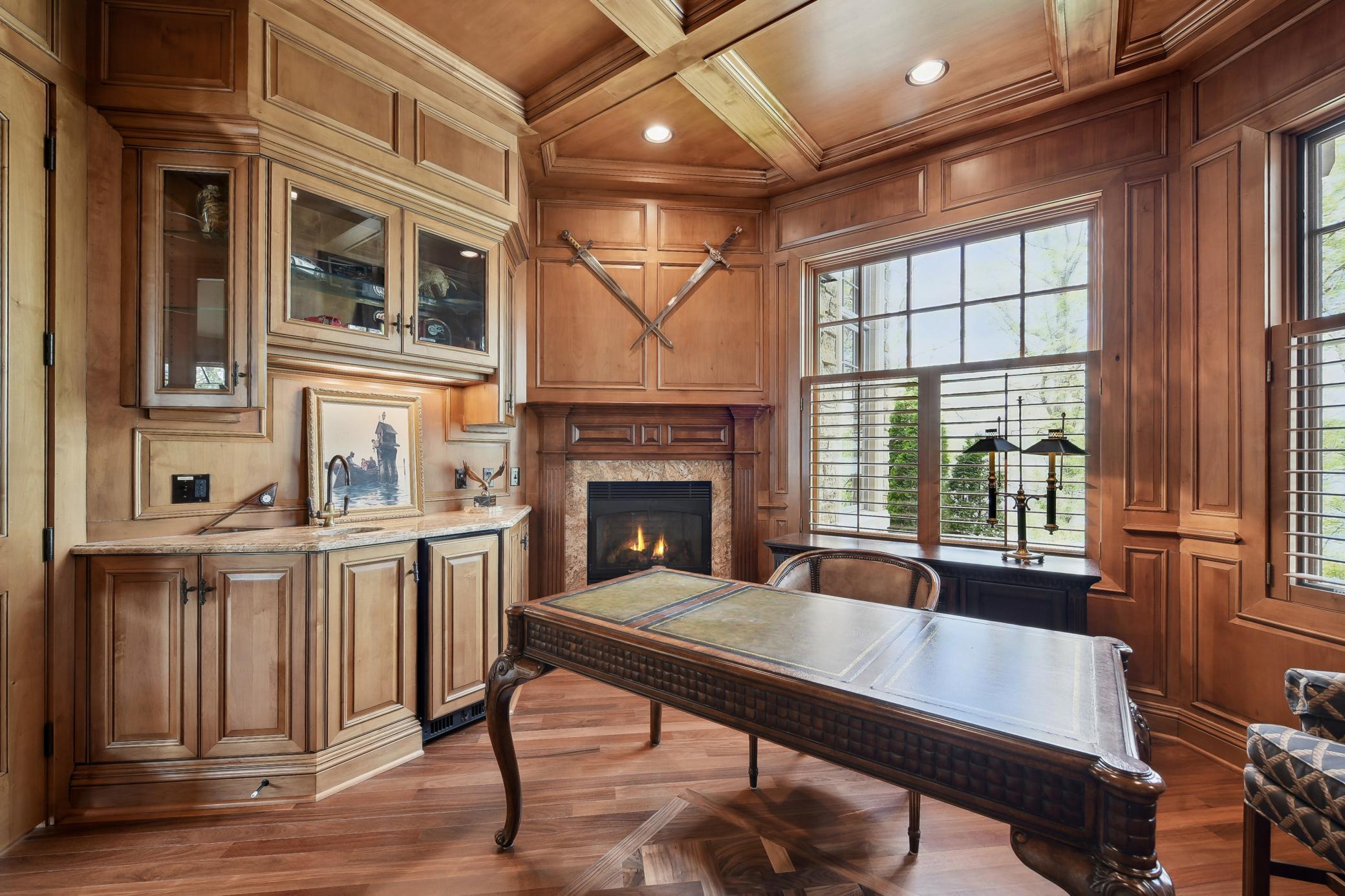 Office features a fireplace, wet bar, mini fridge, & immaculate woodwork and flooring