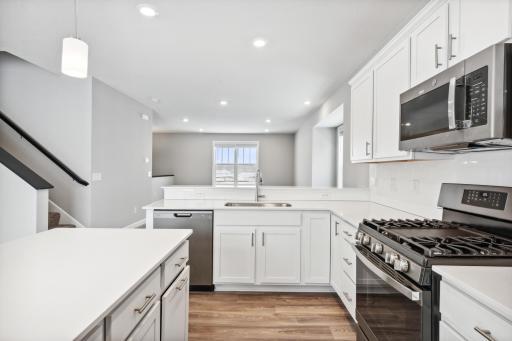 Upgraded kitchen with gas cooking, slate appliances, quartz counertops, white cabinetry and ceramic tile backsplash. Photos are not of actual home. Actual home will be similar. Some colors and features may vary.