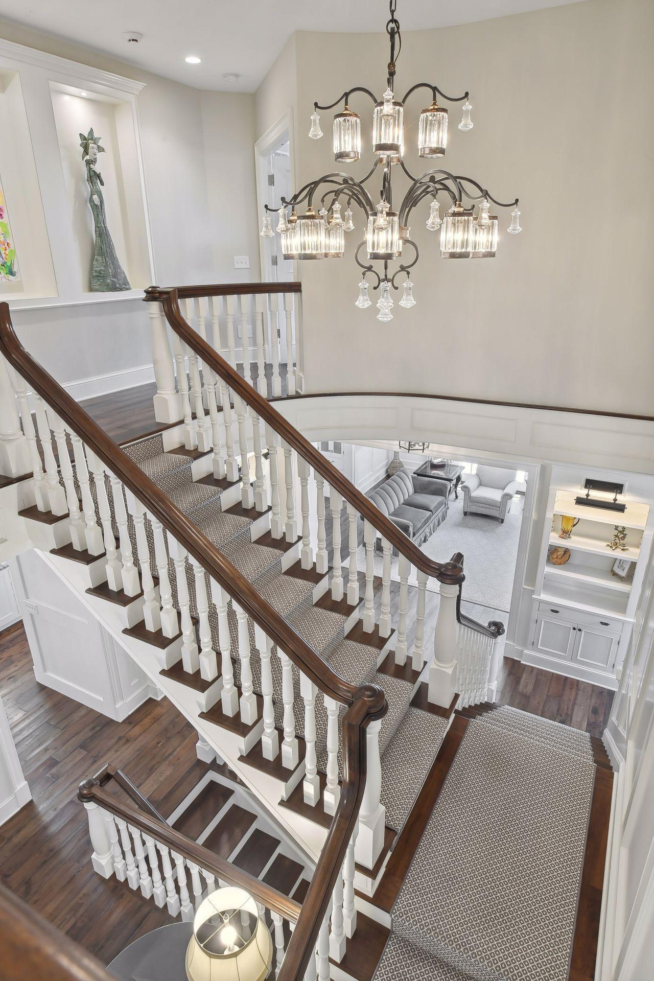 The split staircase features custom designed newel posts and balusters illuminated by this gorgeous light fixture.
