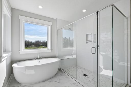 Stunning, modern owner's bathroom with soaker tub, glass enclosed shower and double vanity. White and gray tile detail for a clean and fresh finish.