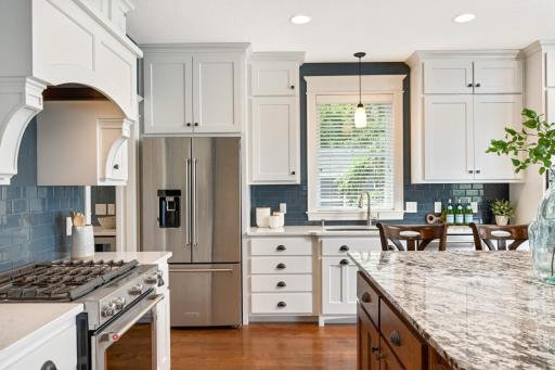 Custom built solid wood enameled cabinets and there is even a hidden knife drawer under the upper cabinet to the right of the refrigerator. Custom wood vent hood above the gas range with a gorgeous glass tiled backsplash.