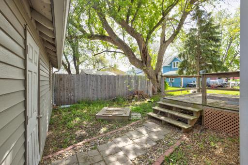 This semi-private backyard is so cute! A brick pathway from deck to garage, partial wood fence, mature tree to provide some coverage from the sun