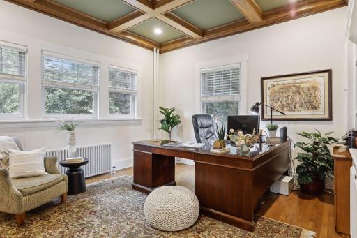 An office/study is adjacent to the front foyer, and features built-ins, a coffered ceiling, and bright windows.