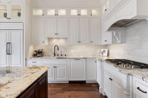 Tiled backsplash, glass cabinets, and under cabinet lighting add to the elegance of the kitchen