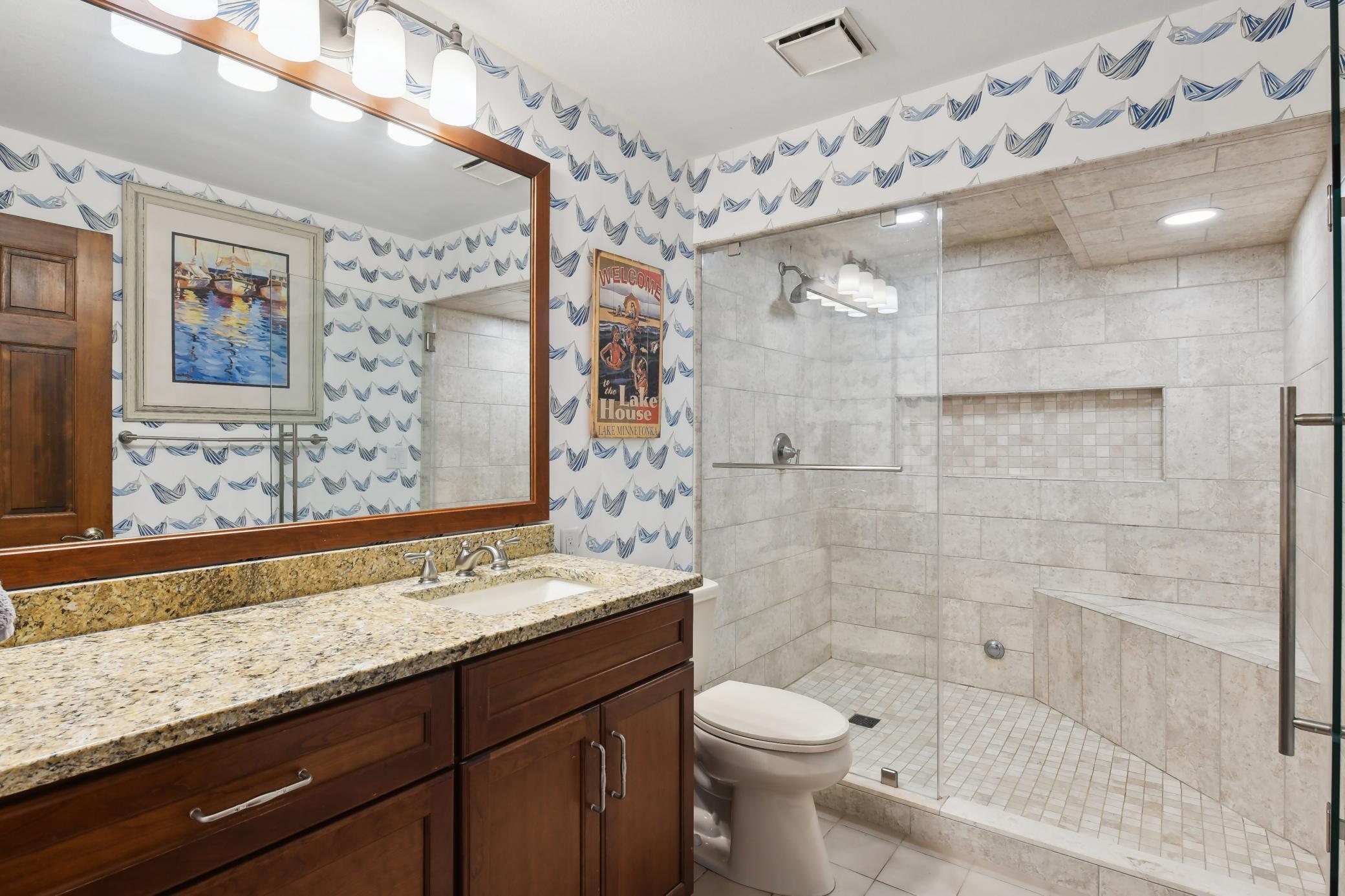 Lower level bathroom offers a steam shower with tile surround and a large vanity with granite counters and framed mirror.
