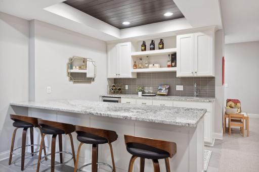 Wet bar with beverage fridge, granite countertops and shiplap ceiling.