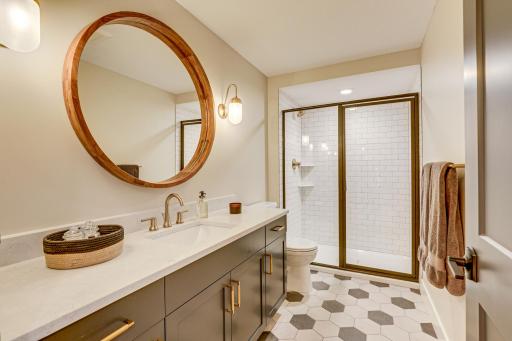 Photo of previously built home. Beautifully designed lower level bath features a gorgeous glass shower with subway tile surround, tile flooring and a large Quartz topped single storage vanity with stylish mirror and sconce lighting.