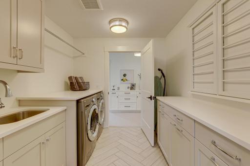 Photo of previously built home. Convenient upper level laundry offers an abundance of storage cabinets, drying rack front load washer and dryer, tile flooring and quartz countertop with undermount sink.