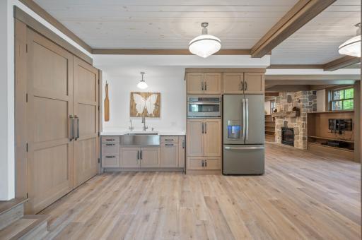This lower-level kitchenette combines the comfort of heated oak floors with the functionality and style of a built-in stainless steel deep sink, quartz countertop, and modern appliances.