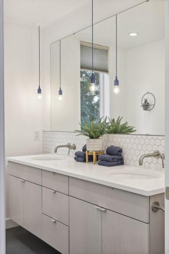 Large double vanity with quartz countertop, tile backsplash and sleek pendant lighting.