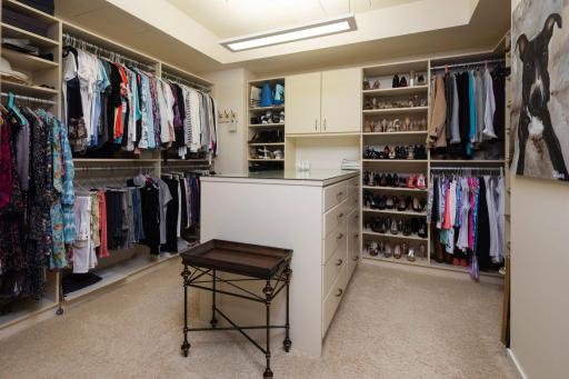 Large custom master closet with glass-topped island feature and multiple drawers.