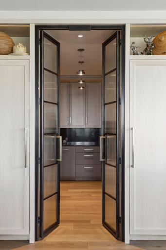 The reeded glass and iron doors are flanked by Sub-Zero refrigerator and freezer. The door handles are ribbed solid brass.